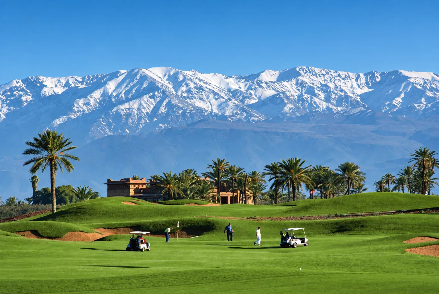 Golfers and buggies on a palm-lined Marrakech fairway with the snow-capped Atlas Mountains behind